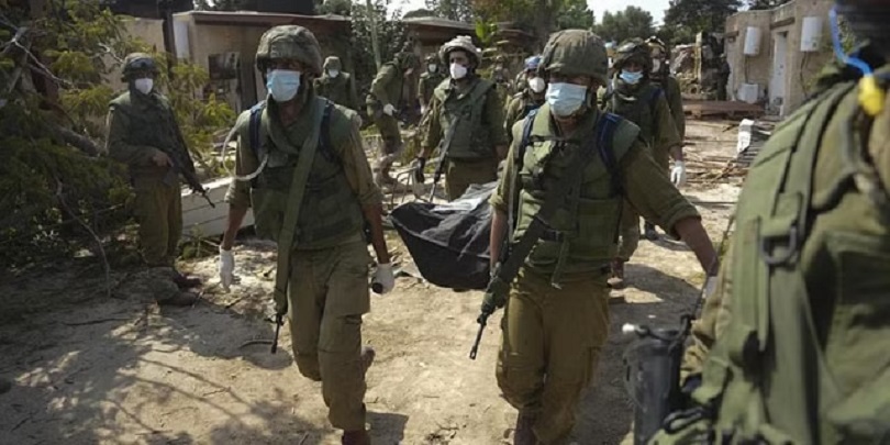 Israeli soldiers carry the body of a person killed in the Hamas attack in kibbutz Kfar Azza. (Photo | AP)